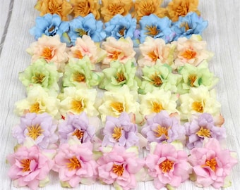 Puede incluir: Surtido de 48 flores artificiales en varios colores, incluyendo amarillo, azul, verde, rosa y morado. Las flores están dispuestas en filas sobre una superficie de madera clara.
