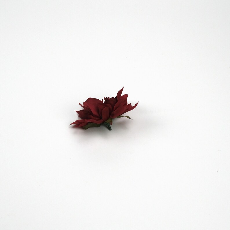 May include: A single red fabric flower with a green stem. The flower is on a white background.