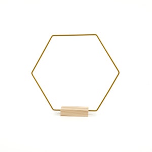 Puede incluir: Un marco hexagonal de alambre dorado con una base de madera. El marco está de pie sobre una superficie blanca.