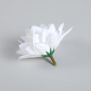 Puede incluir: Una sola flor artificial blanca con un tallo verde. La flor est&aacute; hecha de tela y tiene un aspecto delicado y en capas.