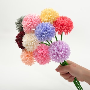 May include: A bouquet of colorful artificial flowers in shades of pink, yellow, red, purple, and blue. The flowers are held together by green stems, creating a vibrant and cheerful arrangement. The flowers are a mix of textures and colors.