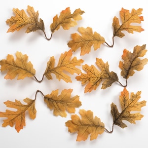 Puede incluir: Hojas artificiales de roble en tonos amarillos, naranjas y marrones, con vetas detalladas. Las hojas están dispuestas sobre un fondo blanco. Estas hojas decorativas son ideales para manualidades y decoración del hogar con temática otoñal.