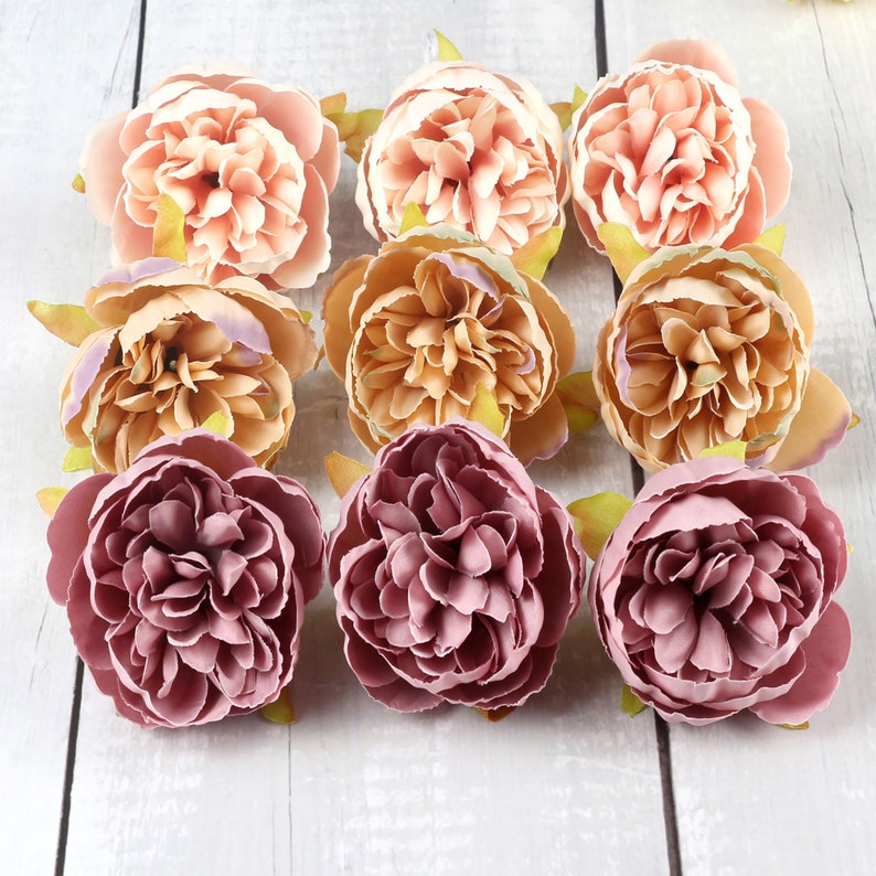 May include: Nine artificial flowers in three different colors: peach, light brown, and mauve. The flowers are arranged in a circle on a white wooden surface.