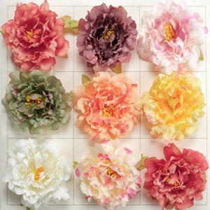 May include: Nine artificial peony flowers in various colors, including pink, peach, white, green, and red. The flowers are arranged in a grid pattern on a white background.
