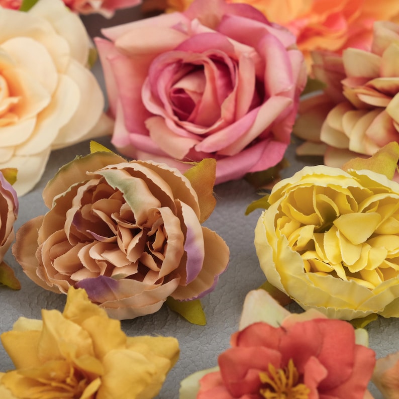 May include: A collection of artificial flowers in various colors, including pink, yellow, peach, and orange. The flowers are in full bloom, with detailed petals and green leaves. The arrangement is suitable for crafts, decorations, or floral arrangements.