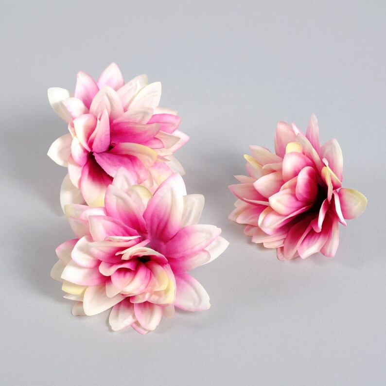 Puede incluir: Tres flores artificiales de color rosa y blanco con p&eacute;talos superpuestos. Las flores est&aacute;n dispuestas sobre un fondo gris.