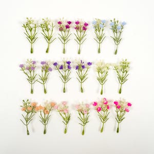 Könnte beinhalten: Eine Sammlung künstlicher Schleierkrautblüten in verschiedenen Farben, darunter Weiß, Lila, Rosa und Blau. Jeder Stiel hat kleine, zarte Blüten und grüne Blätter. Die Blumen sind auf weißem Hintergrund angeordnet.
