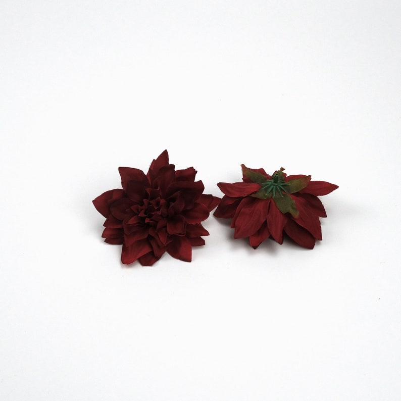 May include: Two burgundy red artificial flowers with a green centre. The flowers are made of fabric and have a realistic appearance.
