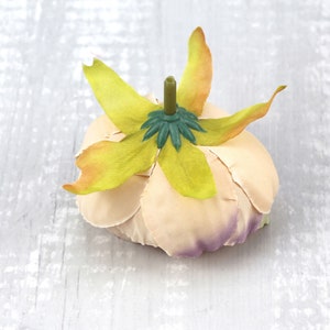 May include: A pale peach-colored fabric flower with a green center and yellow petals. The flower is made of fabric and has a realistic appearance.