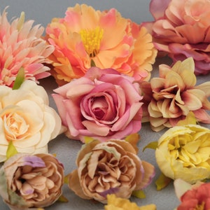 May include: A collection of colorful artificial flowers in shades of peach, pink, and yellow. The arrangement includes roses, peonies, and other floral varieties, with green stems and leaves. The flowers are arranged on a gray surface.