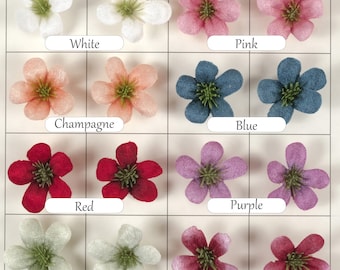 Op de afbeelding: Assortiment van 10 stoffen bloemenversieringen in verschillende kleuren, waaronder wit, roze, champagne, blauw, rood, paars, groen en pruim. Elke bloem heeft vijf bloemblaadjes en een groen centrum.