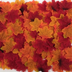 Può includere: Una collezione di foglie autunnali artificiali in tonalità di rosso, arancione e giallo. Le foglie sono realizzate in un materiale sottile e testurizzato e hanno un aspetto realistico.
