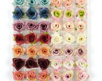 Puede incluir: Una cuadrícula de 36 cabezas de flores de rosa artificiales en varios colores, incluyendo rosa, rojo, azul y crema. Las flores están dispuestas en filas y columnas sobre un fondo blanco.