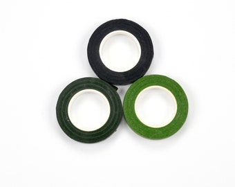 May include: Three rolls of floral tape in black, dark green, and light green, arranged in a triangular pattern. Each roll has a white inner core. The tape is likely used for crafting or floral arrangements.