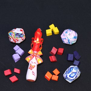 May include: A red, white, and yellow candle with a butterfly design. The candle is surrounded by small, colorful squares and circles.