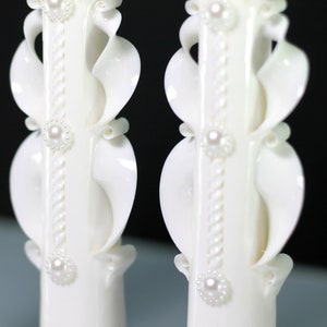 Pu&ograve; includere: Due candele da matrimonio bianche con intricati disegni intagliati e decorazioni di perle.