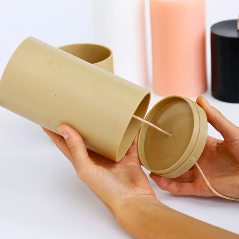 May include: A beige candle container with a lid and a wick. The container is made of a textured material and has a round shape.