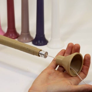 May include: A brown candle making tool with a metal tip and a beige funnel. The tool is used to insert a wick into a candle.
