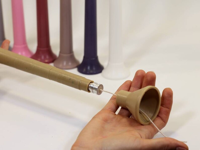 May include: A brown candle making tool with a metal tip and a beige funnel. The tool is used to insert a wick into a candle.