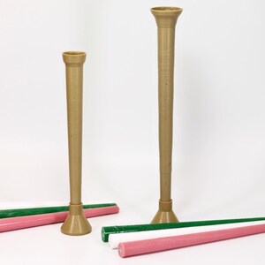 May include: Two brown candle holders of different sizes with a green and pink candle on a white surface.