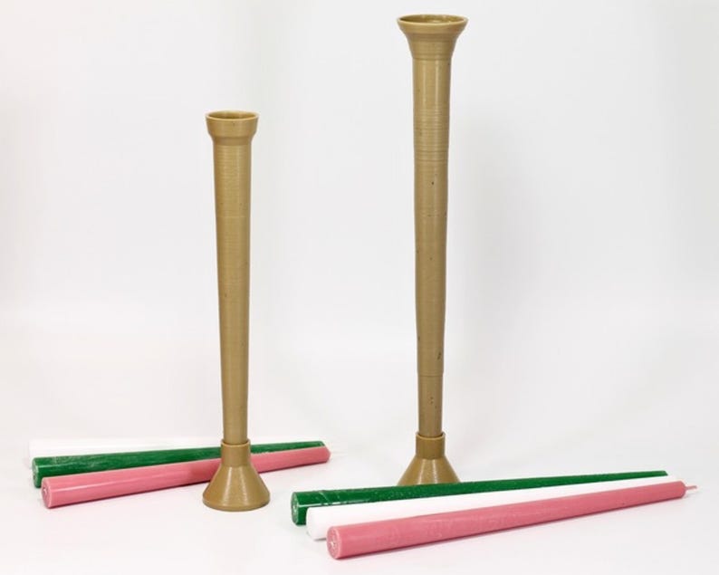 May include: Two brown candle holders of different sizes with a green and pink candle on a white surface.