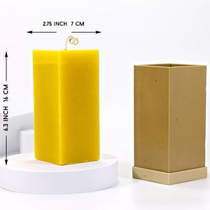 Peut inclure: Une bougie jaune dans un moule à bougie carré brun. La bougie mesure 16 cm de haut et 7 cm de large. Le moule mesure 7 cm de large.