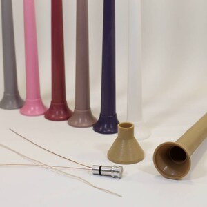 May include: A set of eight colorful plastic tubes with a funnel-shaped opening at the bottom. The tubes are arranged in a row from left to right, with the colors ranging from gray to purple. There are also two brown plastic funnels and a small silver metal connector.