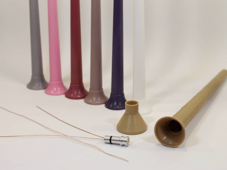 May include: A set of eight colorful plastic tubes with a funnel-shaped opening at the bottom. The tubes are arranged in a row from left to right, with the colors ranging from gray to purple. There are also two brown plastic funnels and a small silver metal connector.