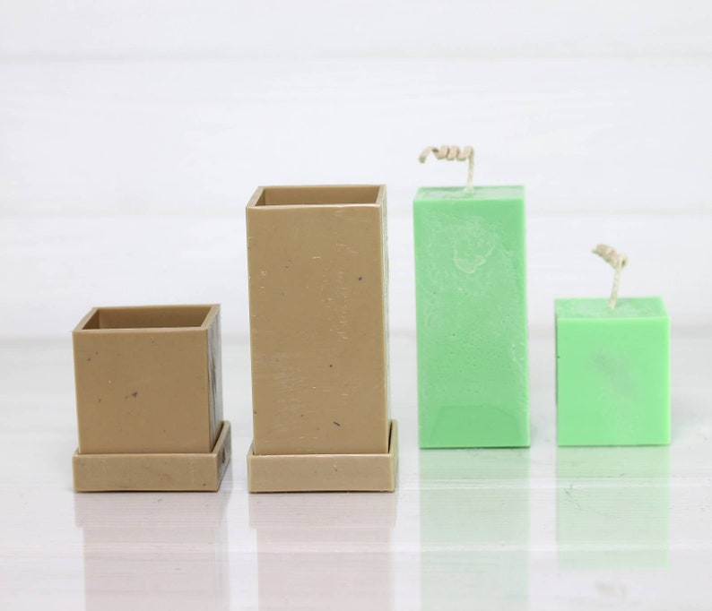 May include: Three candle molds, two are brown and one is green. The brown molds have a base and are square shaped. The green mold is square shaped and has a wick.