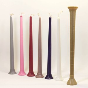 May include: Eight tall candles in various colors, including gray, pink, red, beige, and purple, with white and a brown candle holder.