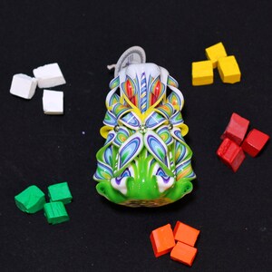 May include: A colorful, hand-carved candle with a green, white, and blue floral design. The candle is decorated with small, iridescent beads.
