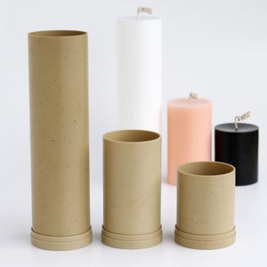 May include: Five candle molds in various sizes. The molds are made of a speckled brown material and have a smooth, cylindrical shape. The molds are arranged in a row on a white surface.