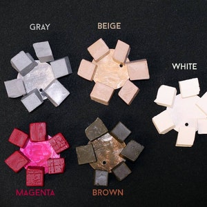 May include: A set of eight color swatches in the colors gray, beige, white, magenta, and brown. Each swatch is a small square with a textured surface.