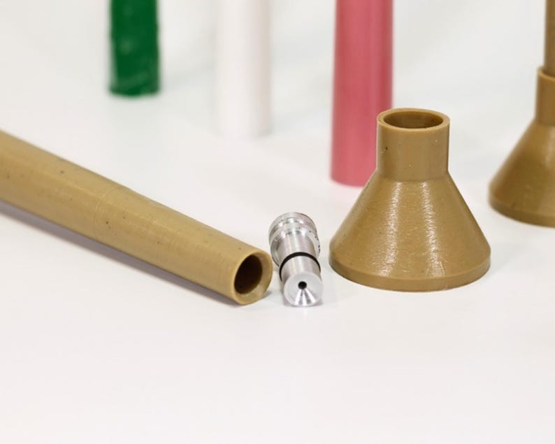 May include: A close-up of a brown plastic funnel with a silver nozzle attached to a brown plastic tube. The funnel is sitting on a white surface.
