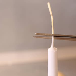 May include: A pair of silver scissors cutting the wick of a white candle.