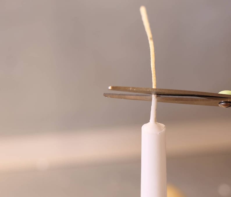 May include: A pair of silver scissors cutting the wick of a white candle.