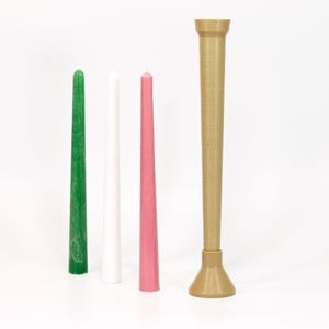 May include: Three taper candles in green, white, and pink, standing next to a brown candle holder.