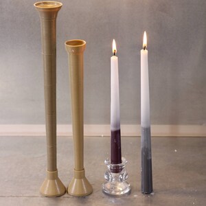 May include: Two brown ceramic candle holders, one taller than the other, and two candles in a glass holder. The candles are white with a purple and gray gradient.