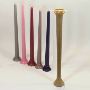 May include: A set of eight tall, slender candles in various colors, including gray, pink, red, purple, and white. The candles have a decorative base and a curled wick.