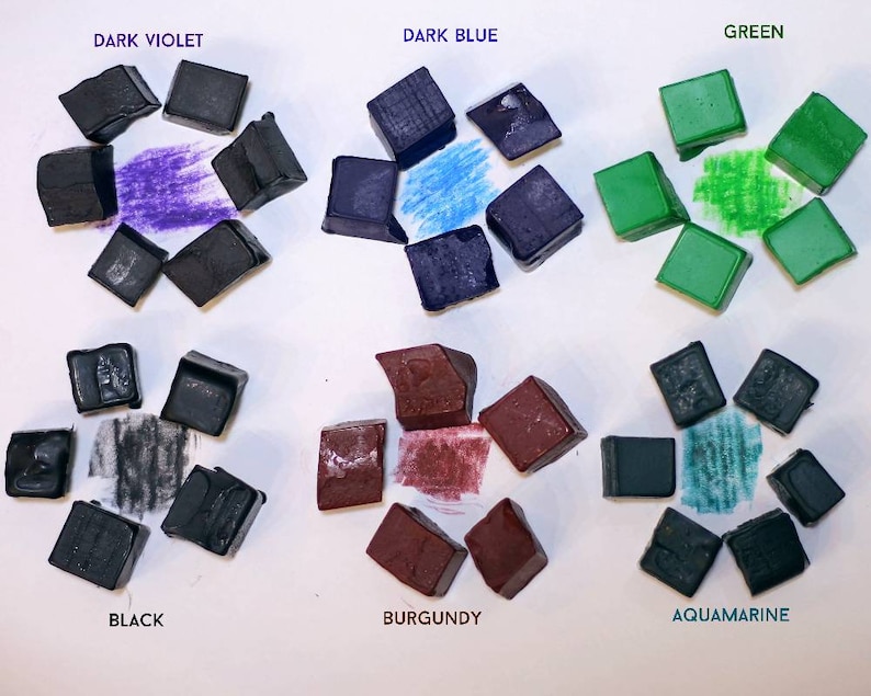 May include: Nine watercolor paint pans in various colors, including dark violet, dark blue, green, black, burgundy, and aquamarine. Each pan is arranged in a circle with the color name printed above it.