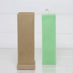 May include: A beige rectangular candle mold with a removable base next to a green pillar candle.