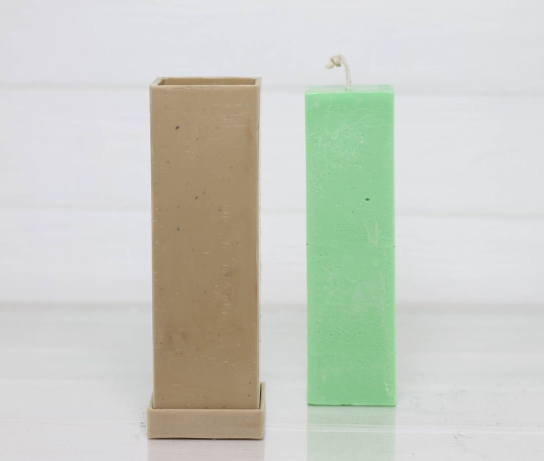 May include: A beige rectangular candle mold with a removable base next to a green pillar candle.