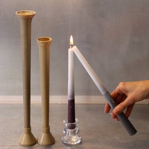 May include: Two brown ceramic candle holders with a white candle in a glass holder. The candle is lit and the flame is visible. A hand is holding a second white candle.