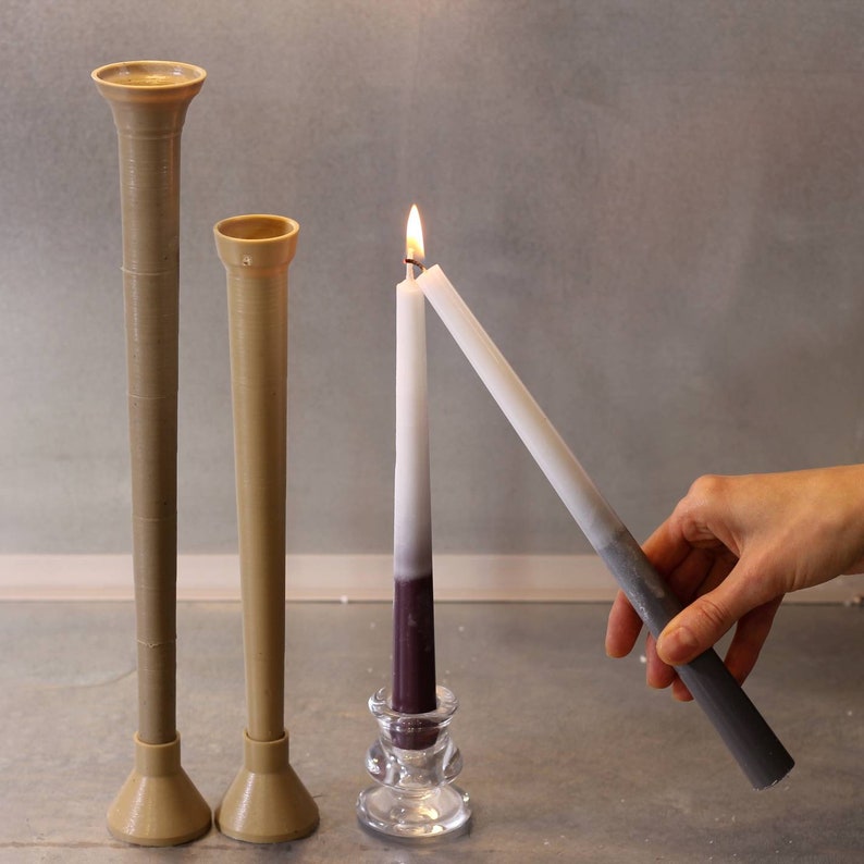 May include: Two brown ceramic candle holders with a white candle in a glass holder. The candle is lit and the flame is visible. A hand is holding a second white candle.