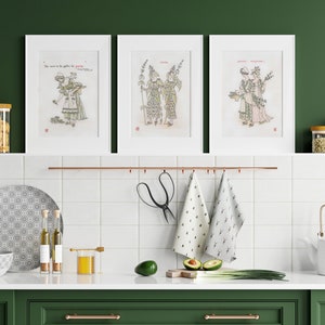 Puede incluir: Tres grabados art&iacute;sticos enmarcados con ilustraciones de figuras con vestimenta de &eacute;poca. Los grabados se exhiben sobre una encimera de cocina con varios art&iacute;culos de cocina, incluyendo frascos, un plato, un cuenco y una tetera. La cocina tiene una combinaci&oacute;n de colores verde y blanco.