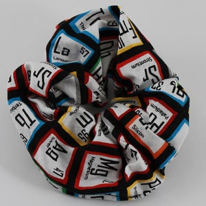 May include: A white, black, red, blue, and yellow fabric scrunchie with a pattern of colorful squares containing the chemical symbols and names of elements.