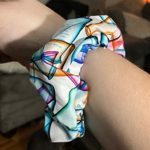 May include: A white scrunchie with a colorful geometric pattern featuring blue, pink, orange, and green accents.