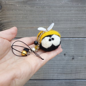 Può includere: Un portachiavi a forma di ape in feltro con occhi neri, strisce gialle e nere e ali bianche. Il portachiavi ha una catena argentata con perline nere e dorate.