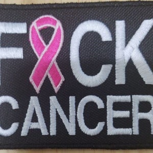 May include: Black fabric patch with white embroidered text "F*CK CANCER" and a pink ribbon.