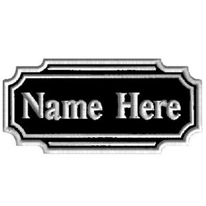 May include: A rectangular black sign with a decorative border and the words "Name Here" in a white, serif font. The sign has a classic, elegant design, suitable for a business or home.